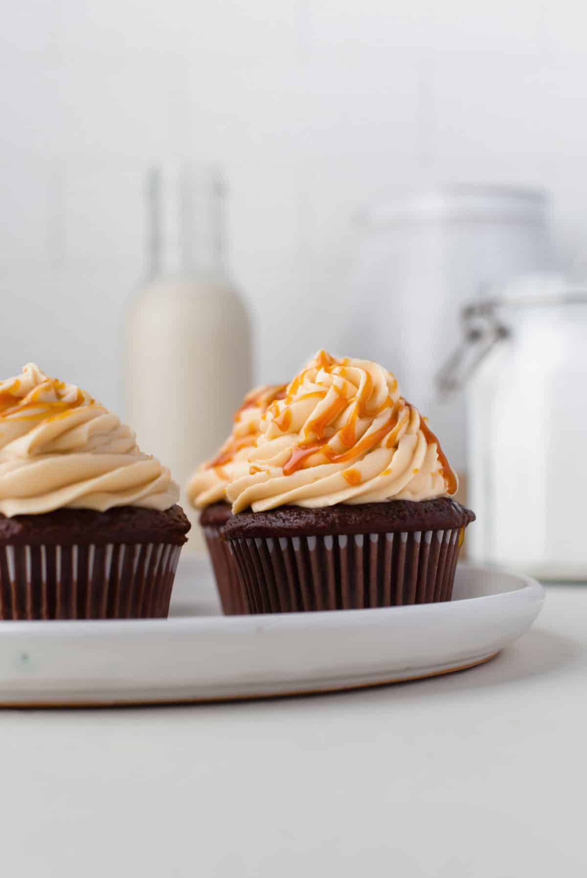 A white plate with three chocolate cupcakes topped with salted caramel frosting. 