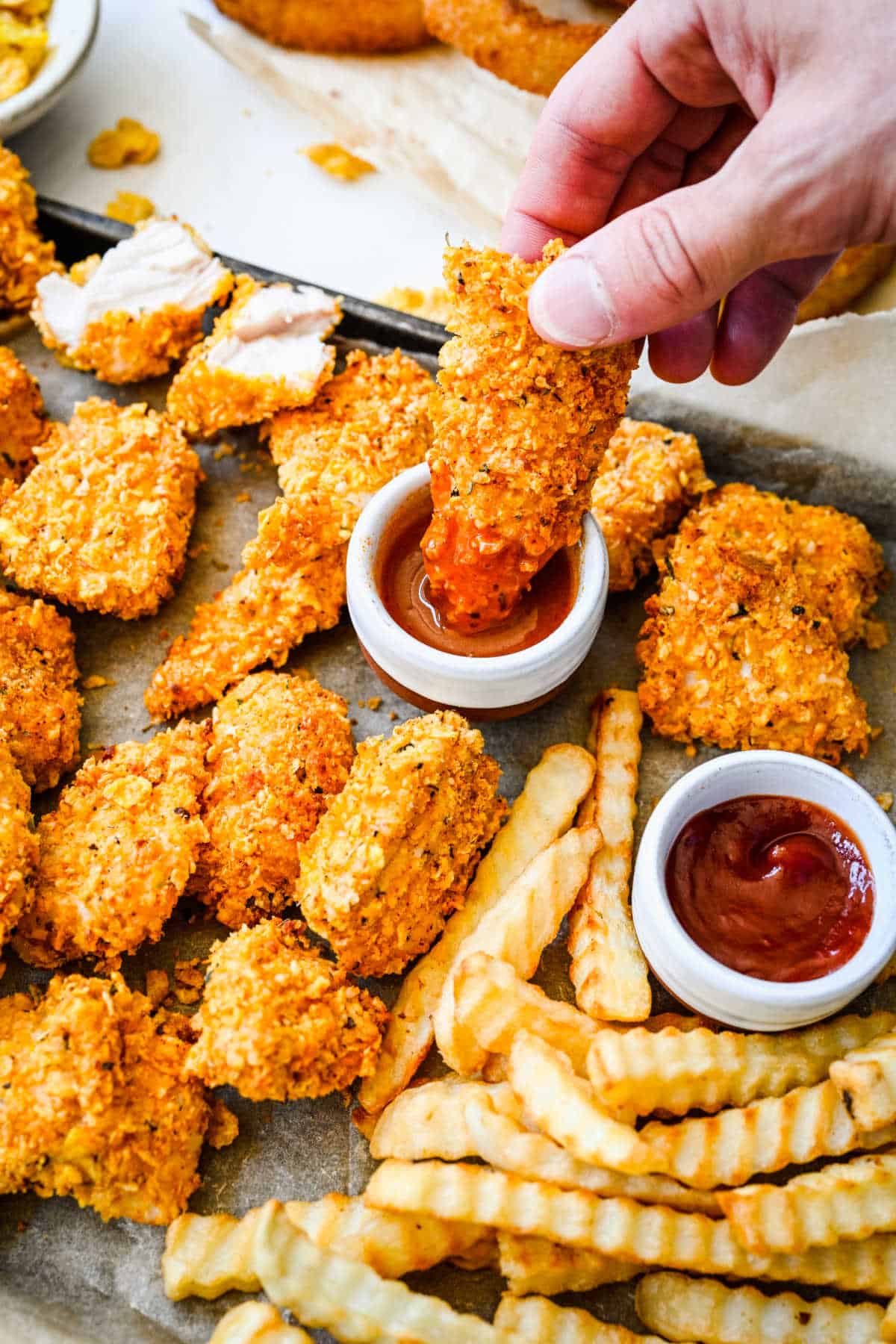 A hand dipping a chicken nugget into a dish of buffalo sauce.