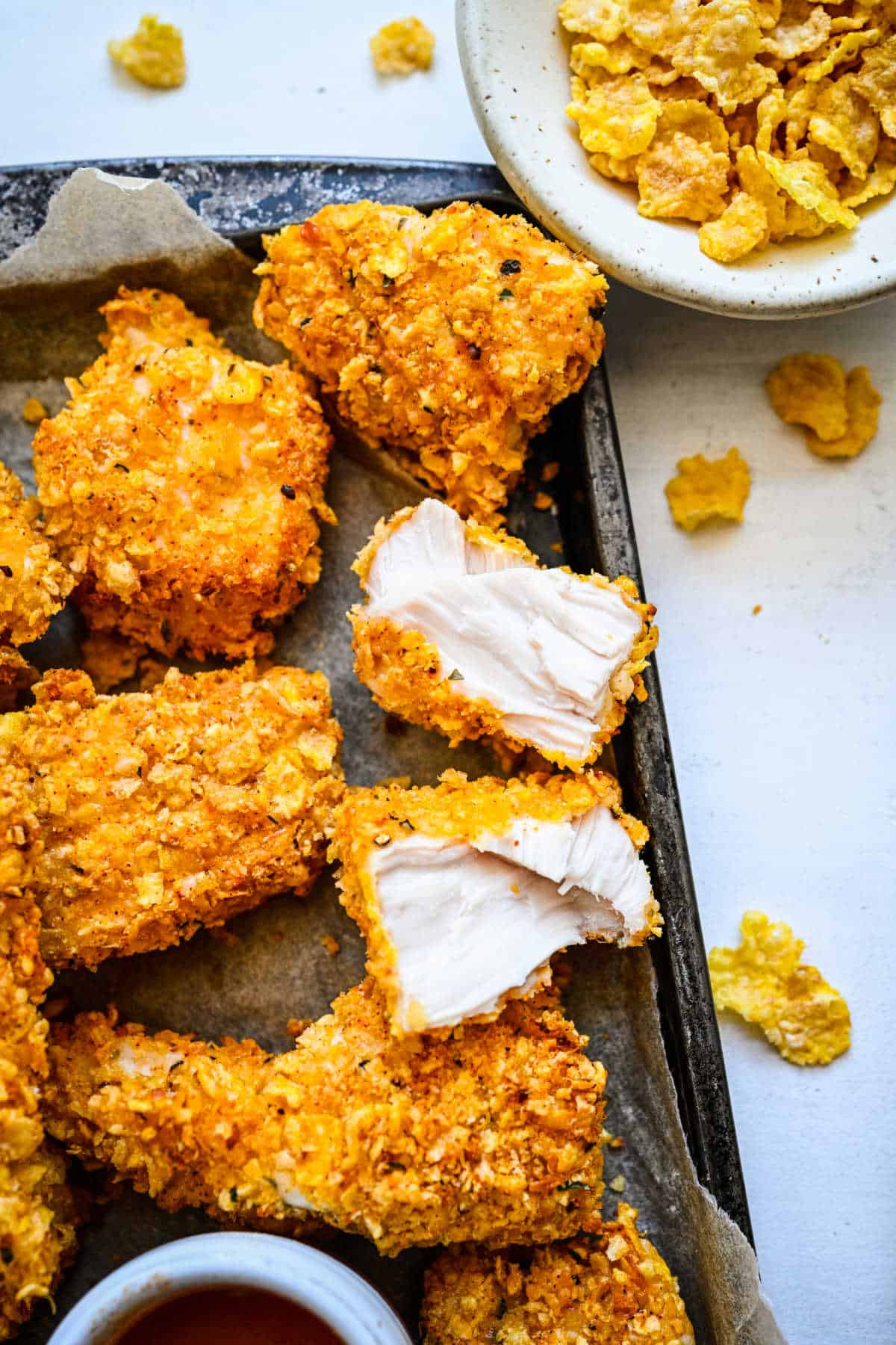 A chicken nugget cut in half next to other chicken nuggets on a baking sheet. 