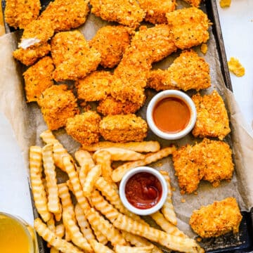 A large baking sheet with crunchy baked chicken nuggets and french fries on it.