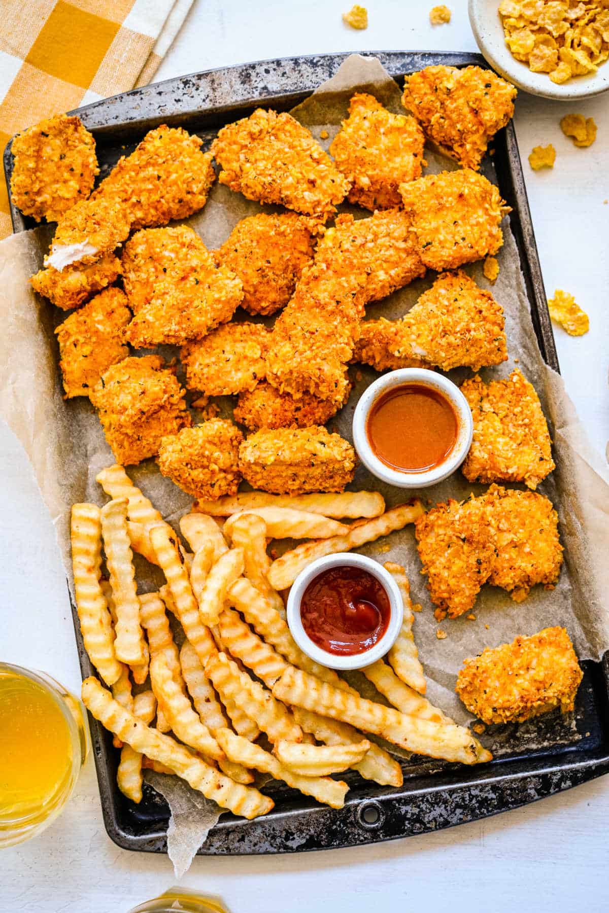 A large baking sheet with crunchy baked chicken nuggets and french fries on it. 