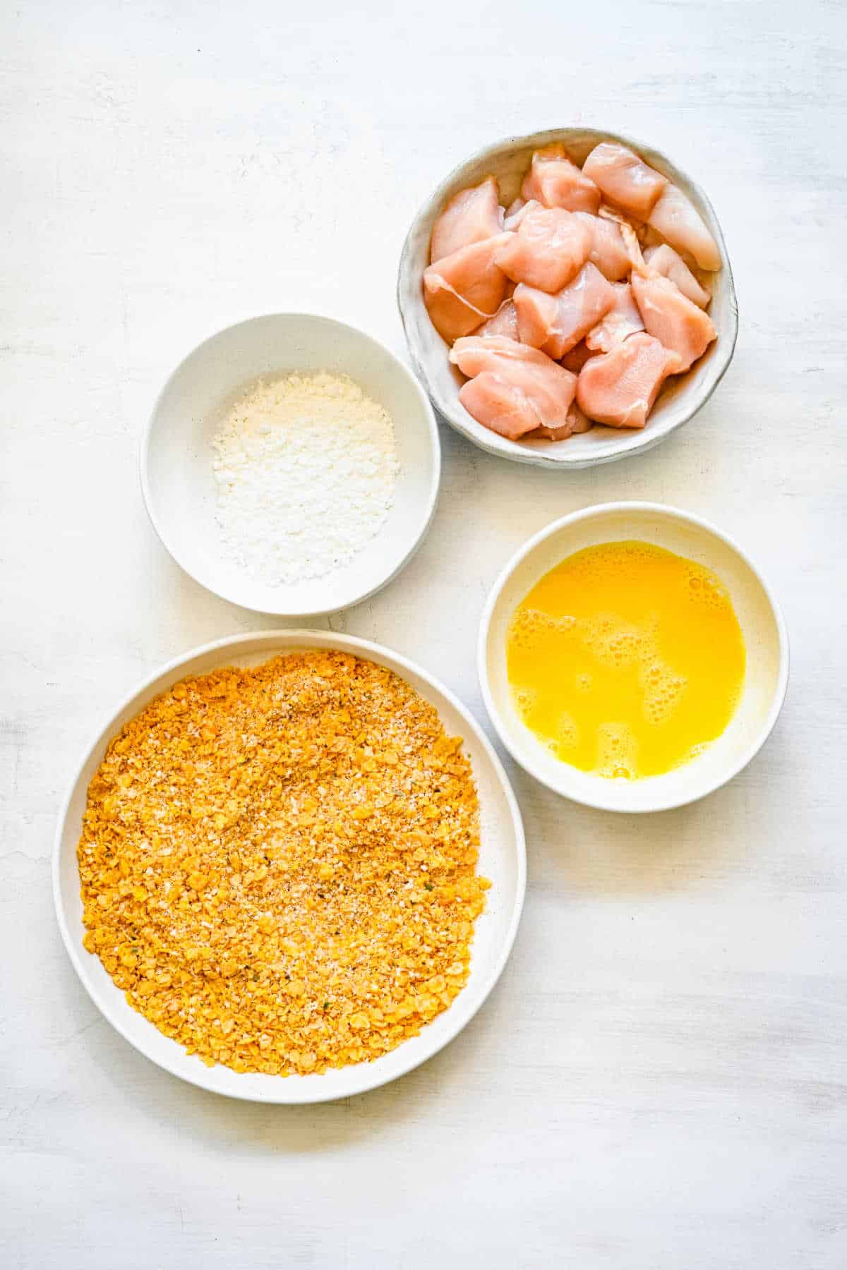 Dishes of cornflake coating egg and cornstarch in dishes. 
