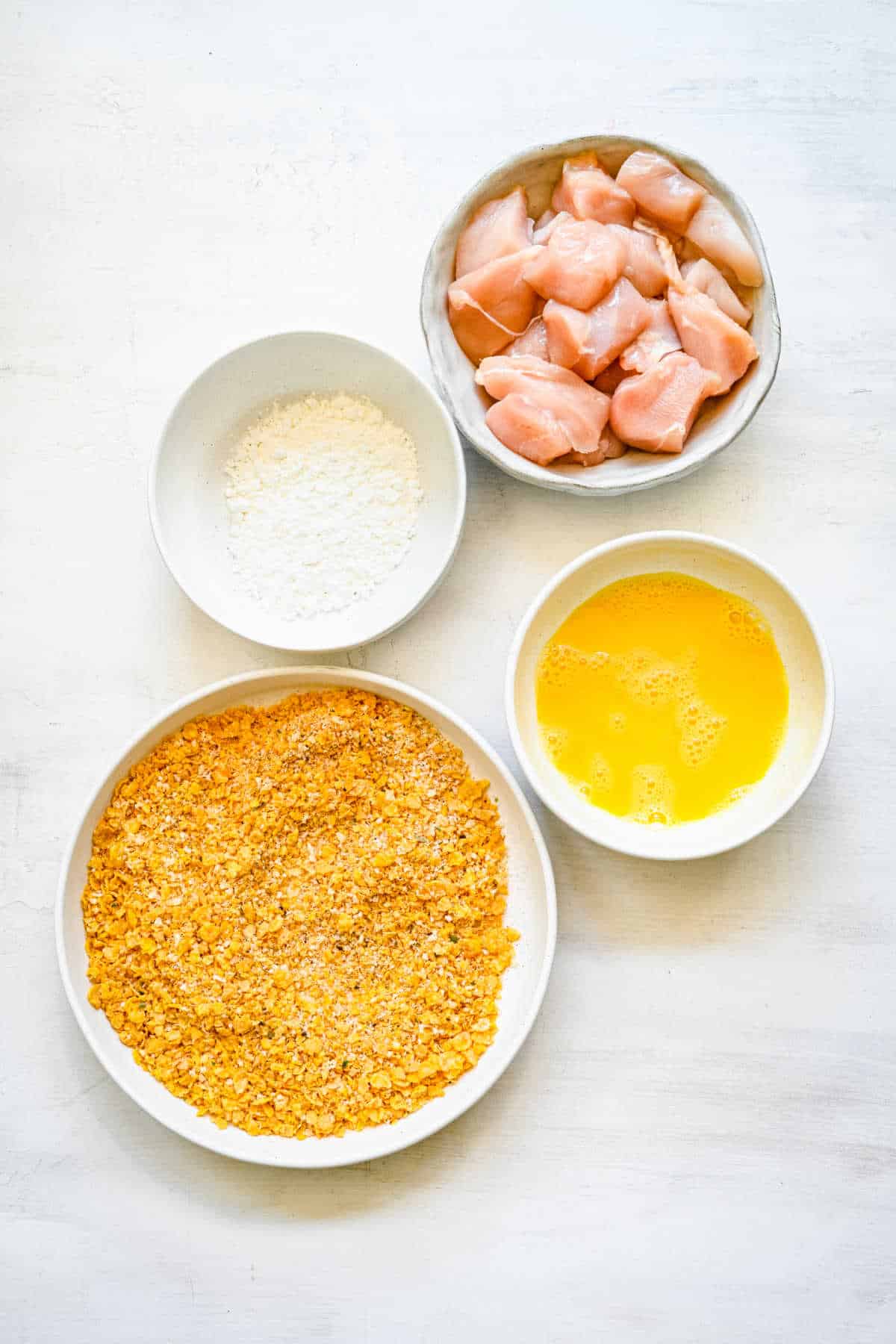 Dishes of cornflake coating egg and cornstarch in dishes.