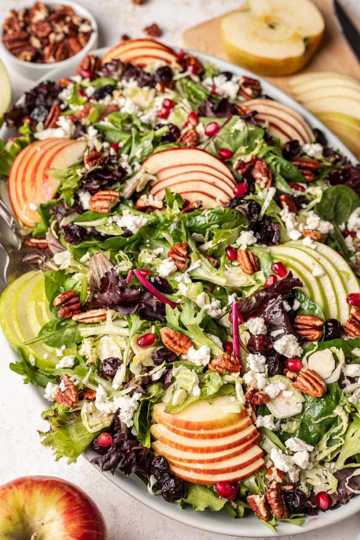 Fall harvest salad next to a dish of toasted pecans and sliced apples. 