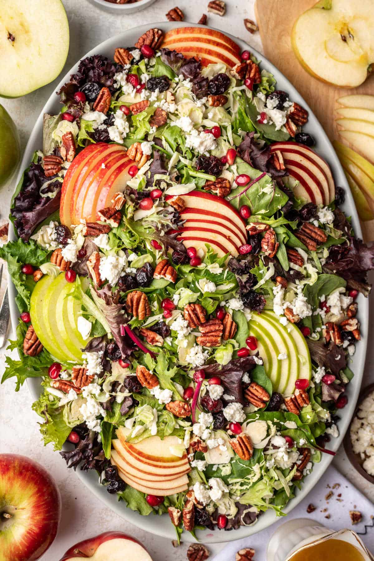 A fall harvest salad surrounded by pieces of sliced apple and apples. 