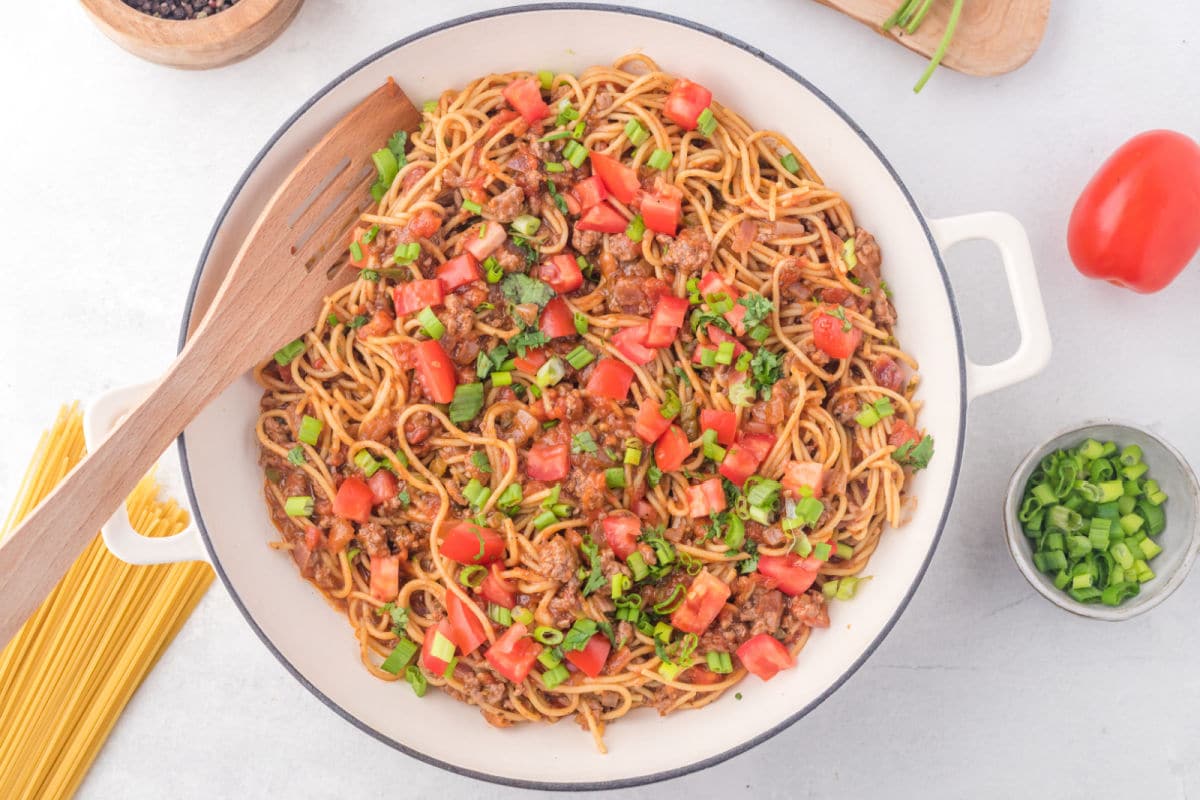 A white skillet of taco spaghetti with a wooden spatula in it.