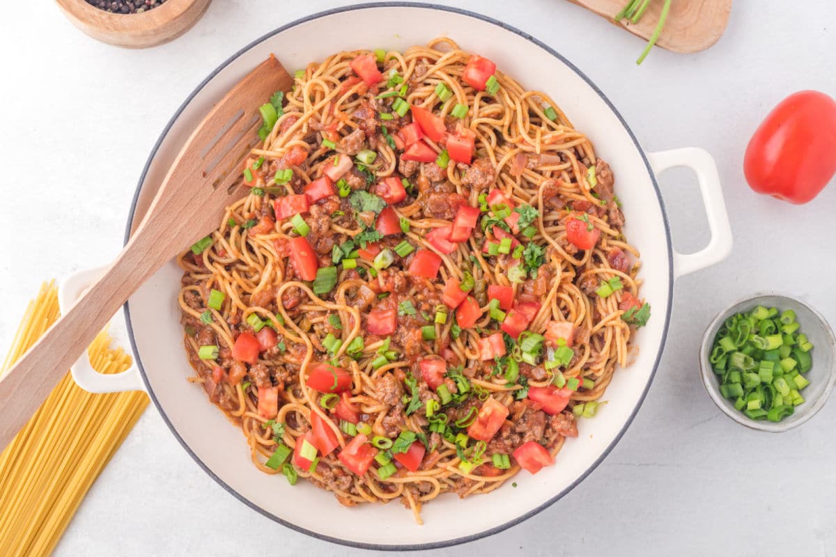 A white skillet of taco spaghetti with a wooden spatula in it. 