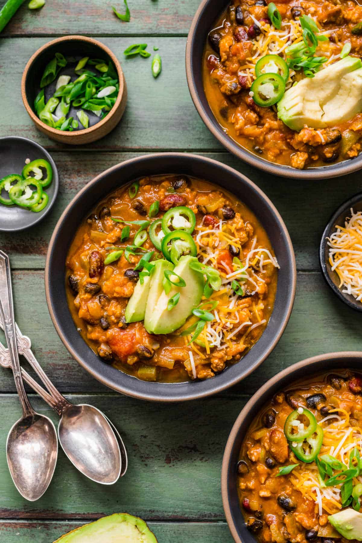 A bowl of pumpkin turkey chili surrounded by dishes of jalapeno and green onion.