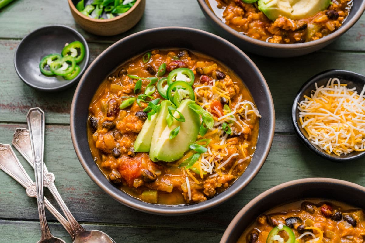 A bowl of turkey pumpkin chili next to silver spoons.