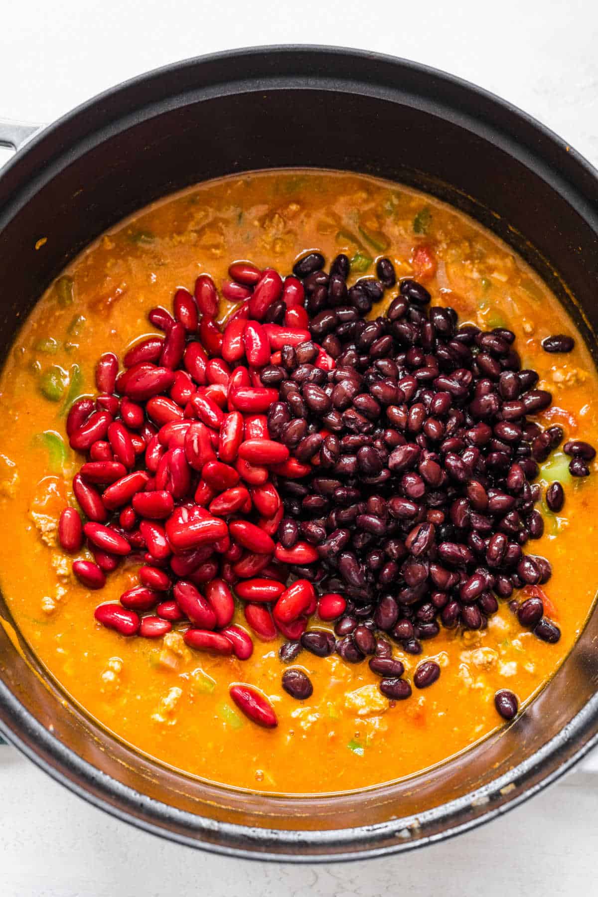Black beans and kidney beans sitting on top of turkey chili in a pot.