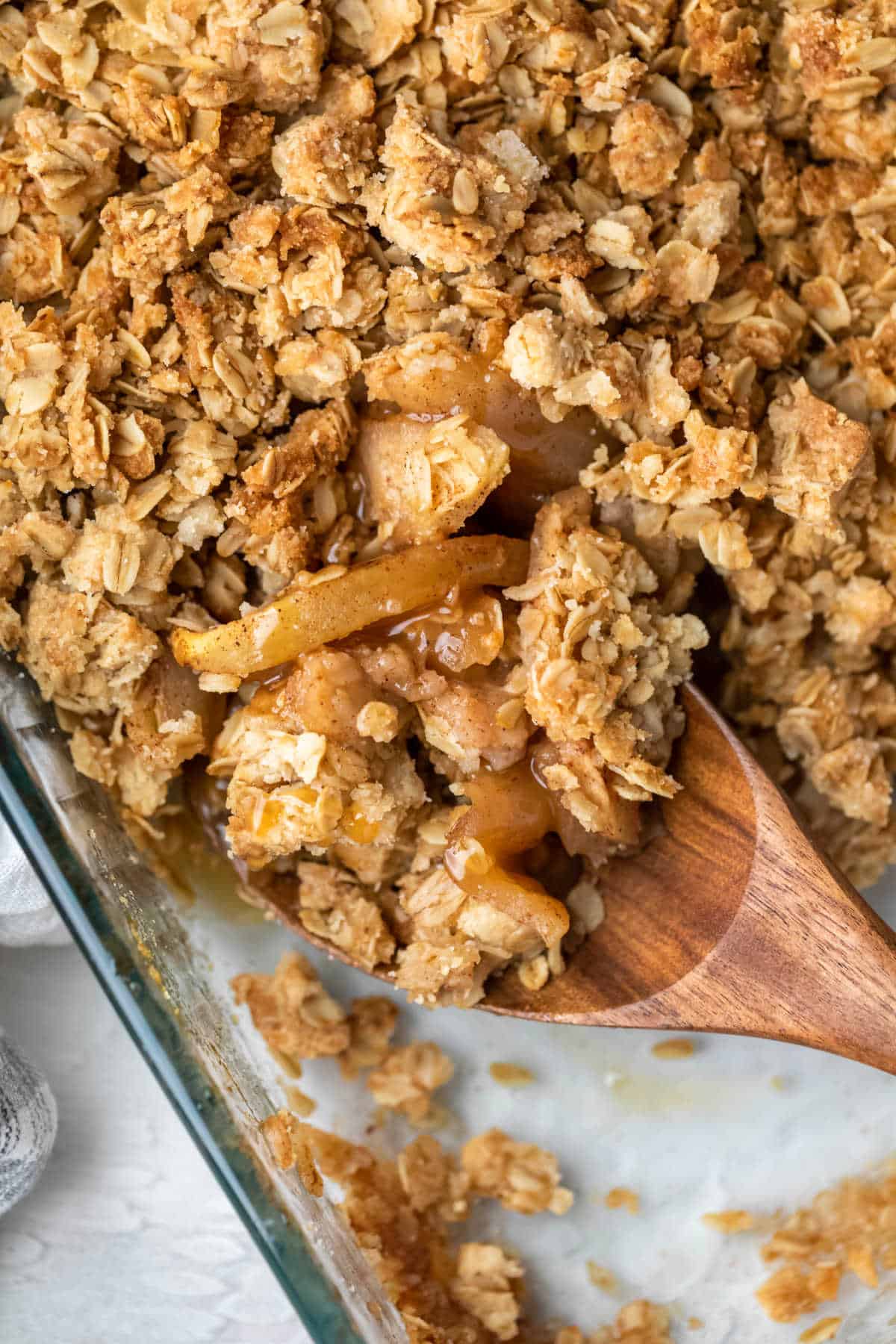 A wooden spoon scooping up apple crisp from a baking dish.