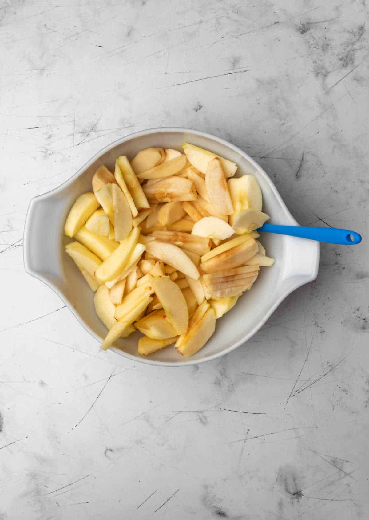 A white mixing bowl full of apple spices and a blue spatula. 