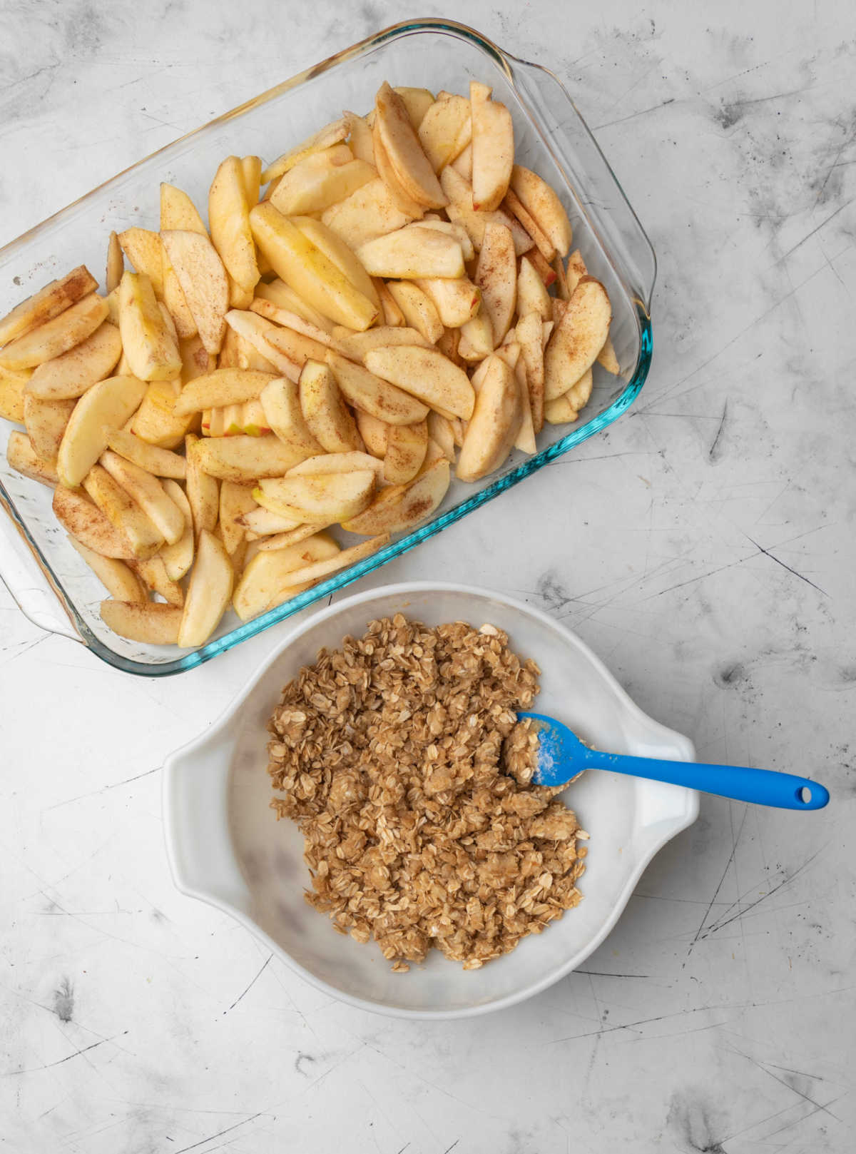 A bowl of apple crisp topping next to a pan of apples. 
