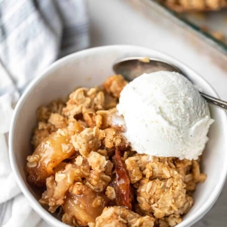 A dish of apple crisp topped with a scoop of vanilla ice cream.
