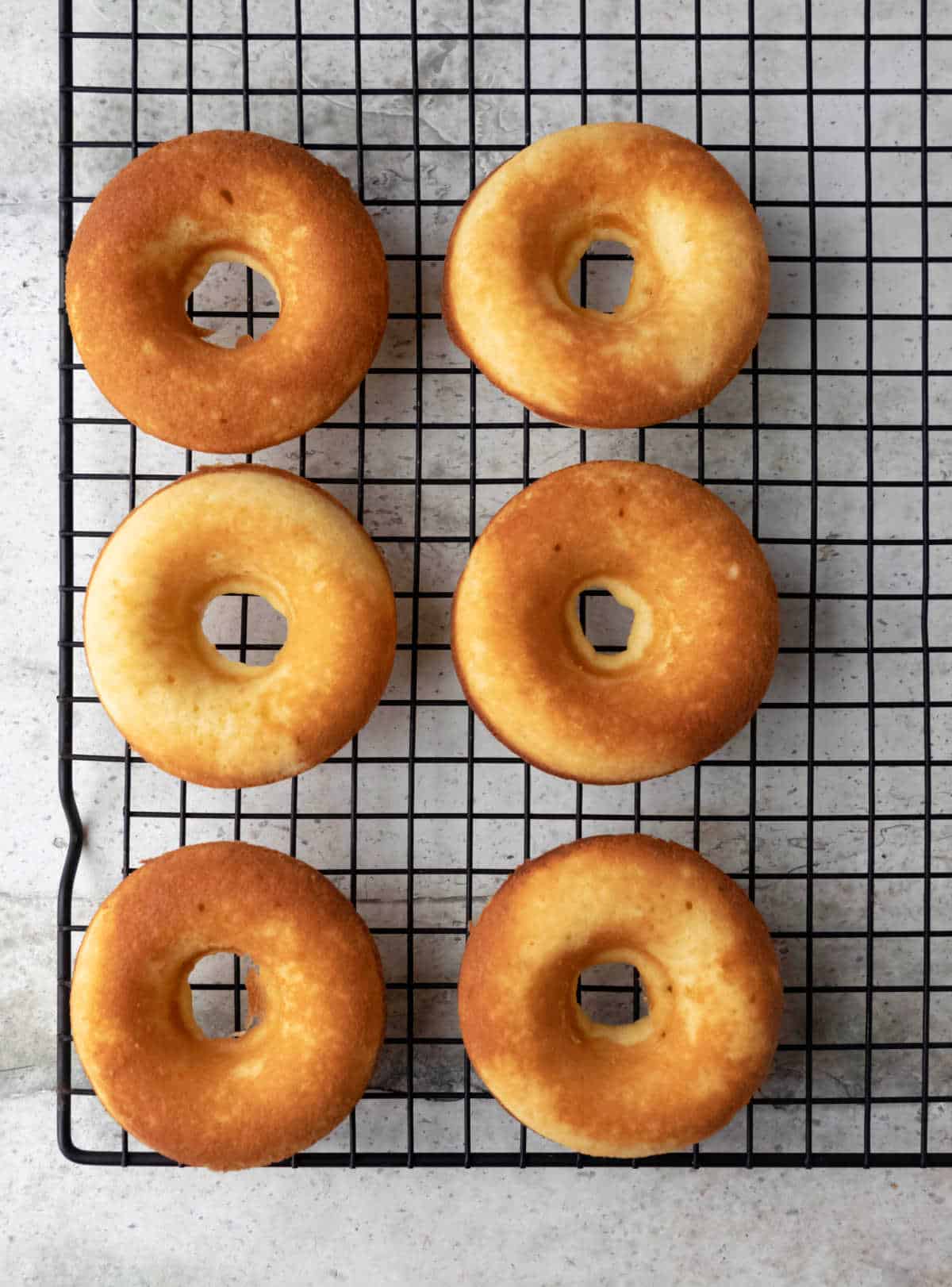 Six baked vanilla donuts on a wire cooling rack. 
