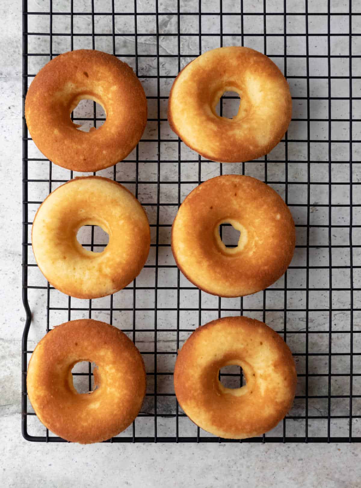 Six baked vanilla donuts on a wire cooling rack.