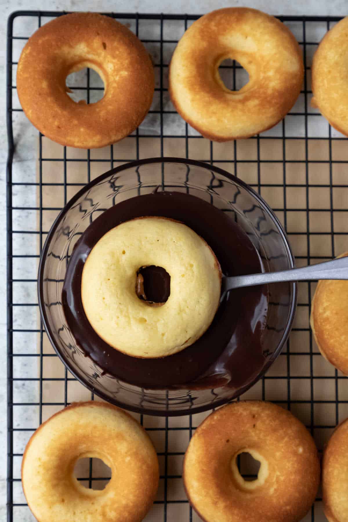 A donut upside down in a bowl of chocolate glaze. 
