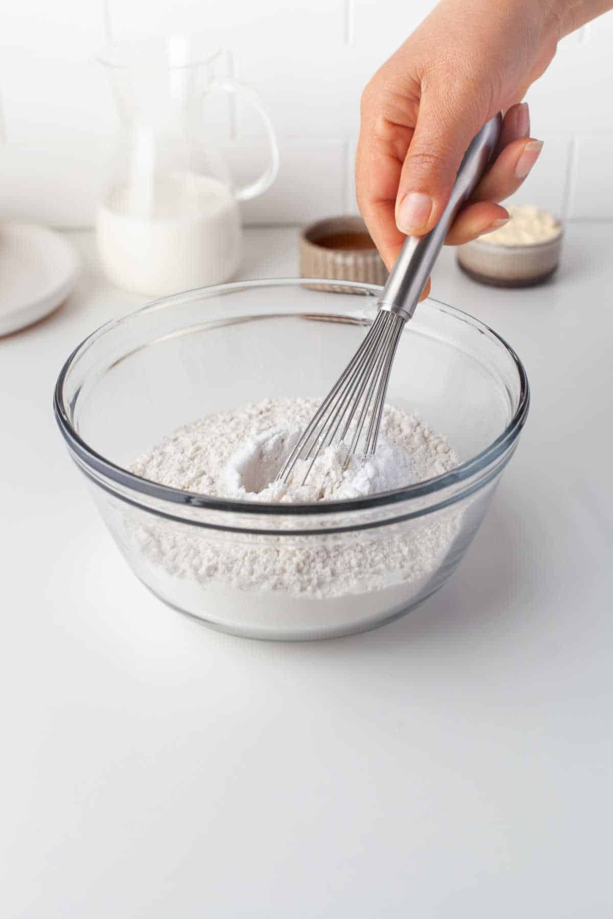 A hand whisking dry ingredients together in a glass mixing bowl. 