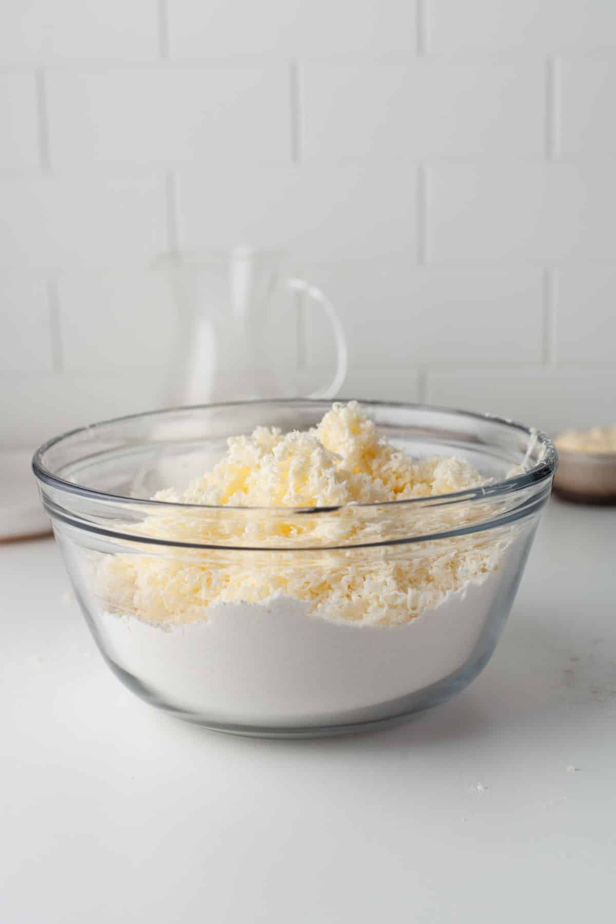Grated butter on dry ingredients in a mixing bowl. 