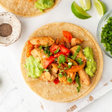 Two chicken fajitas on a white serving board.