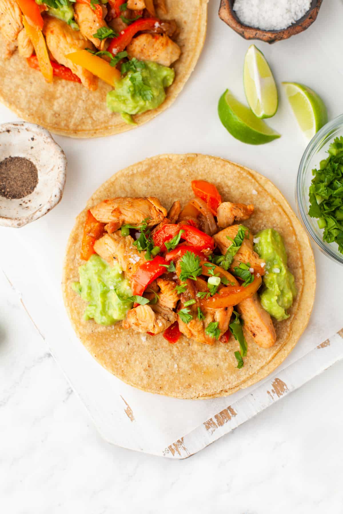 Two chicken fajitas on a white serving board.