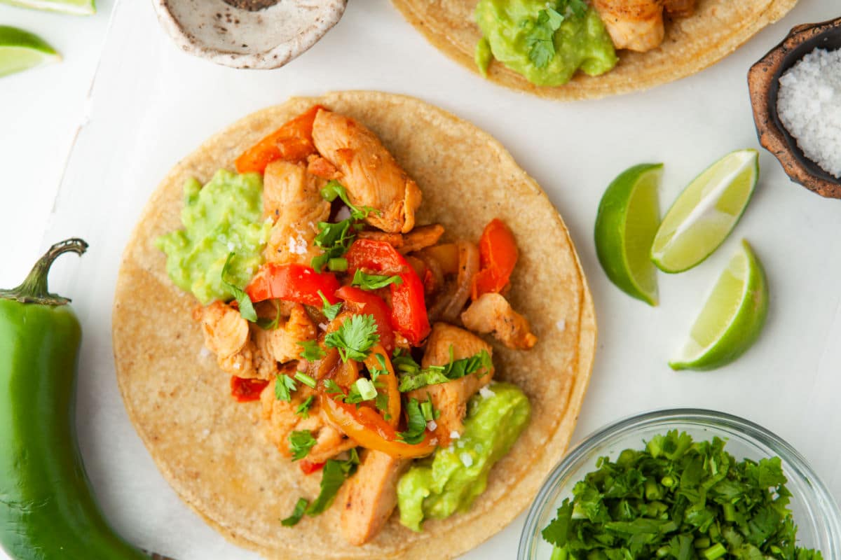 Close up photo of an open chicken fajita topped with fresh cilantro and guacamole.