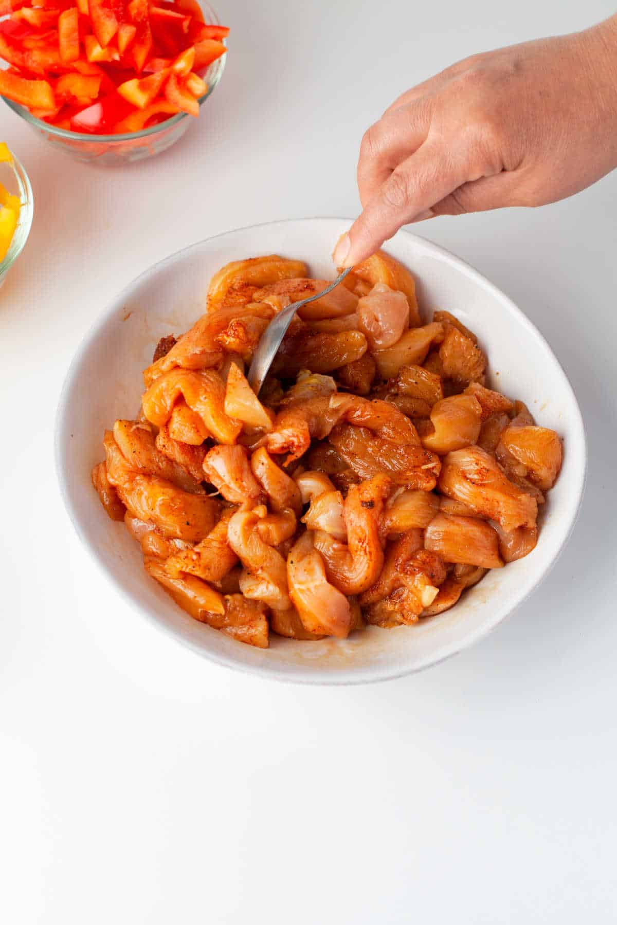 A spoon stirring chicken strips in fajita marinade. 