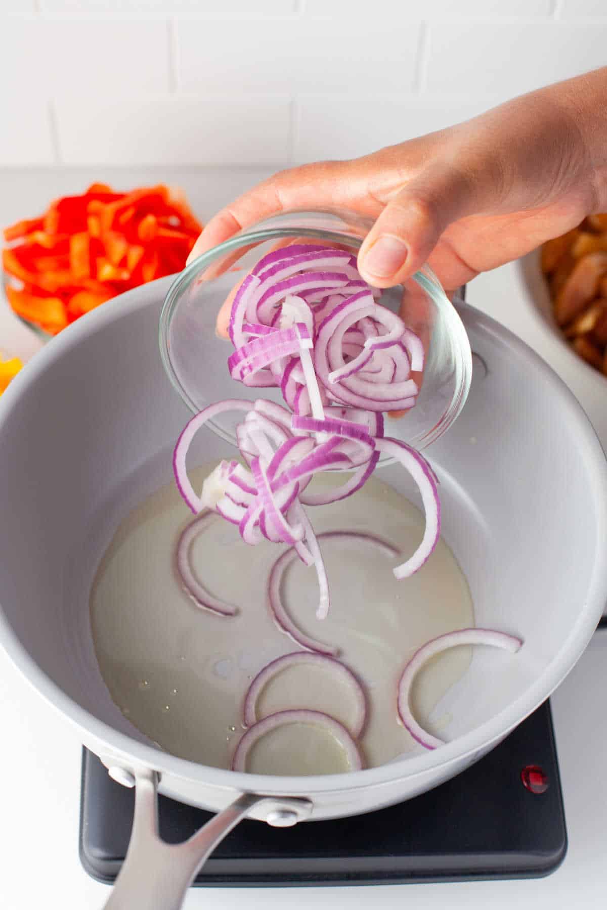 Half moon slices of red onion falling into a pan with hot oil.