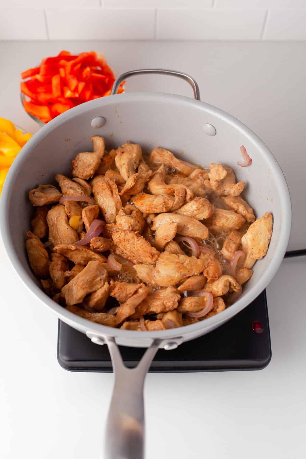 Chicken strips and onion cooking in a skillet.