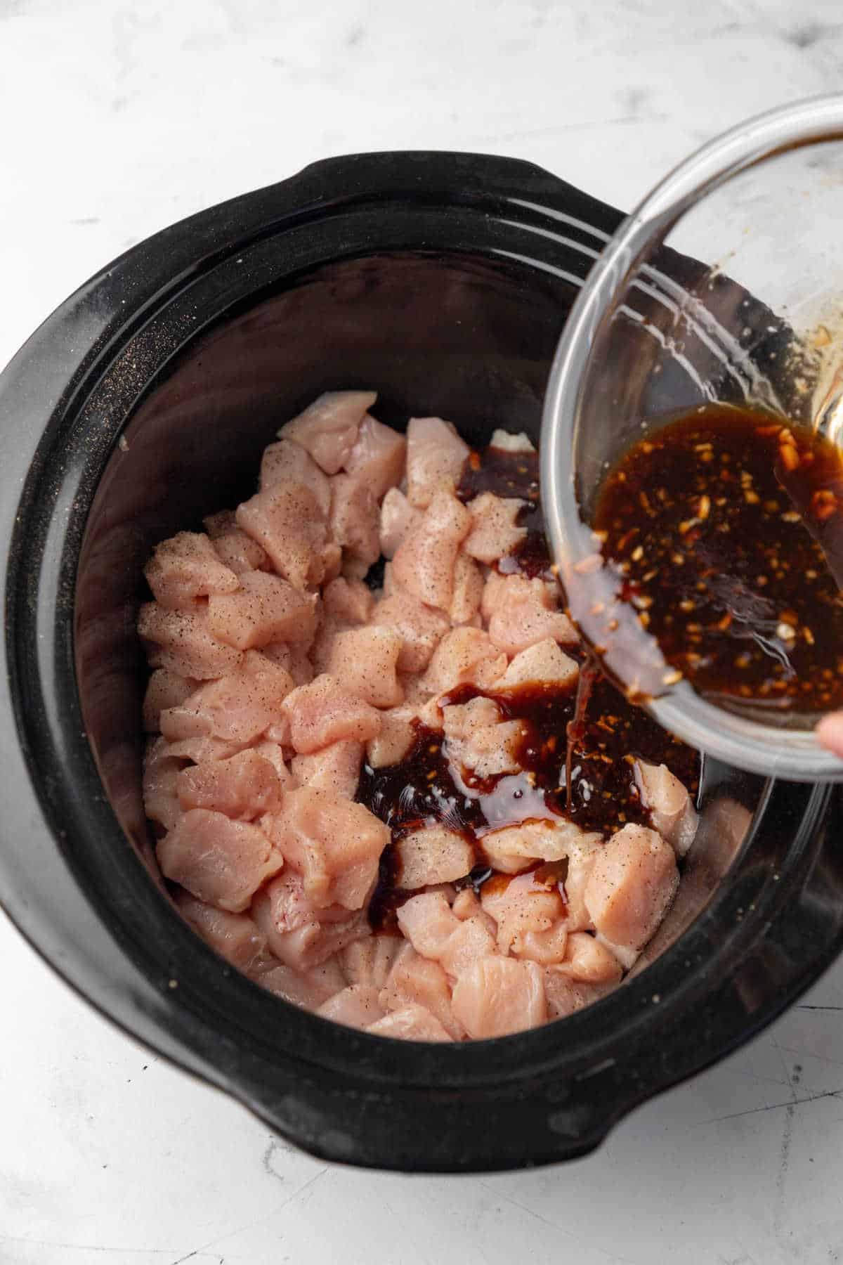 Sesame chicken sauce pouring onto cut up chicken in a slow cooker. 