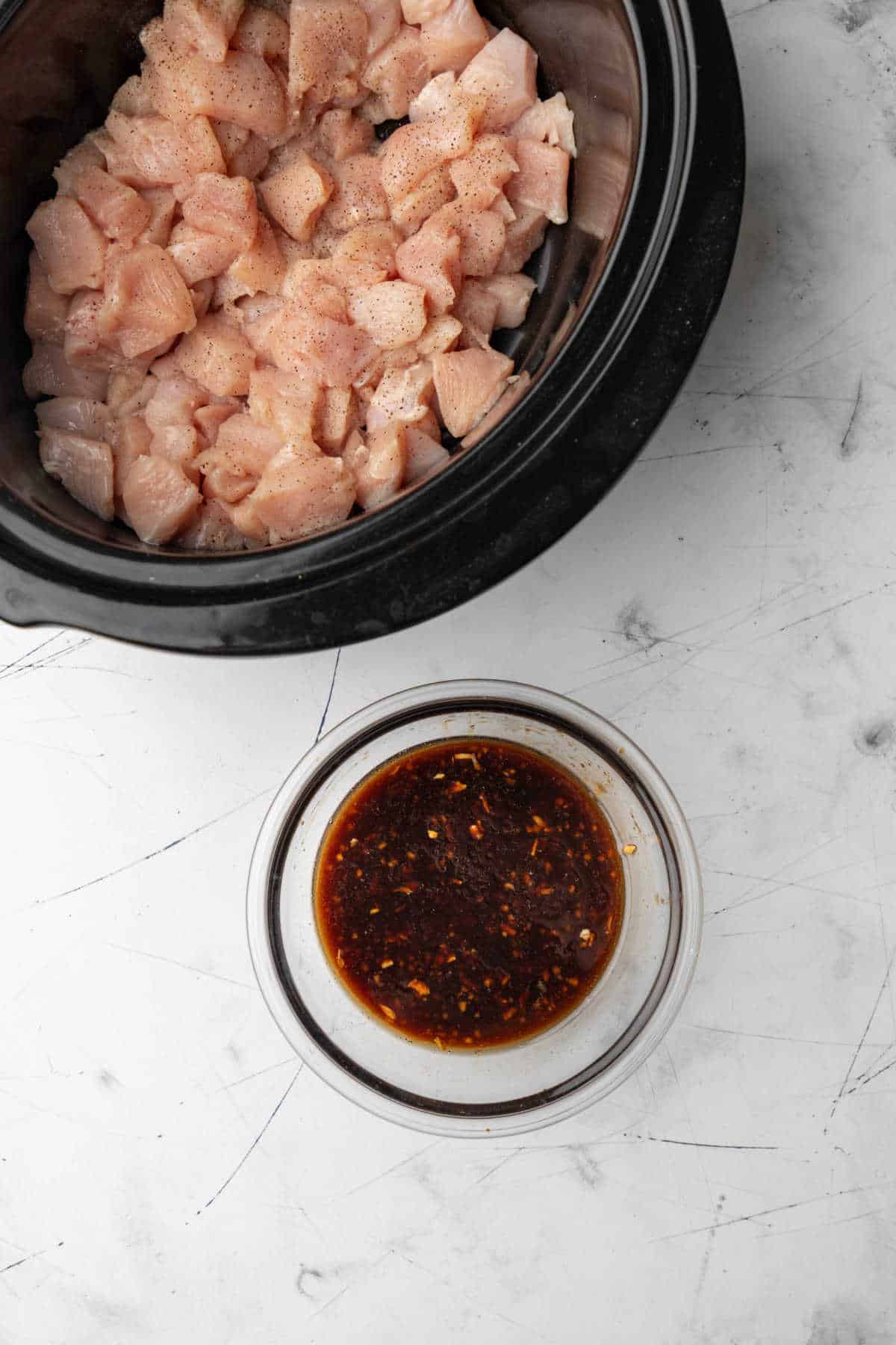 Sesame chicken sauce in a glass mixing bowl next to a crock pot. 