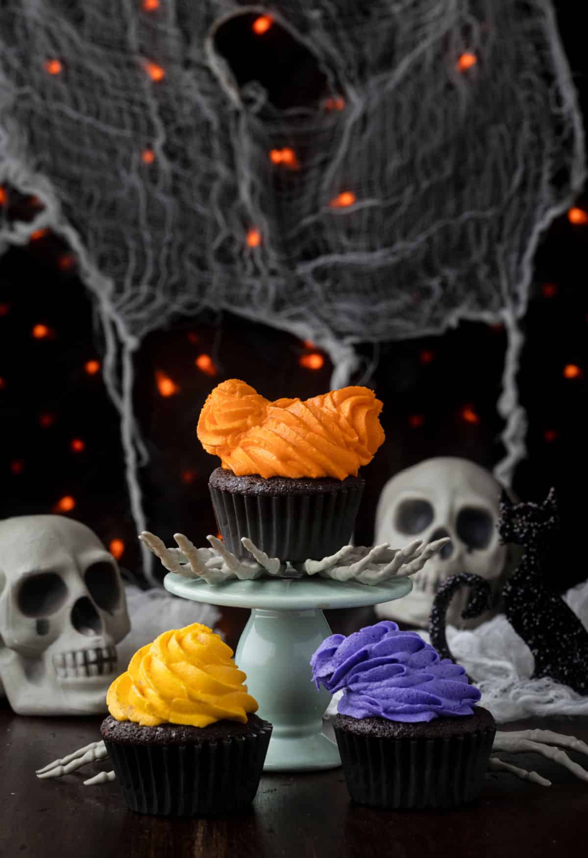 Three hocus pocus cupcakes by plastic skulls and spider webs. 