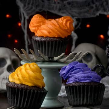Three hocus pocus cupcakes sitting on skeleton hands.