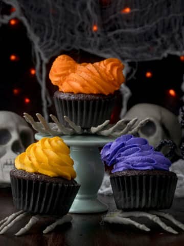 Three hocus pocus cupcakes sitting on skeleton hands.