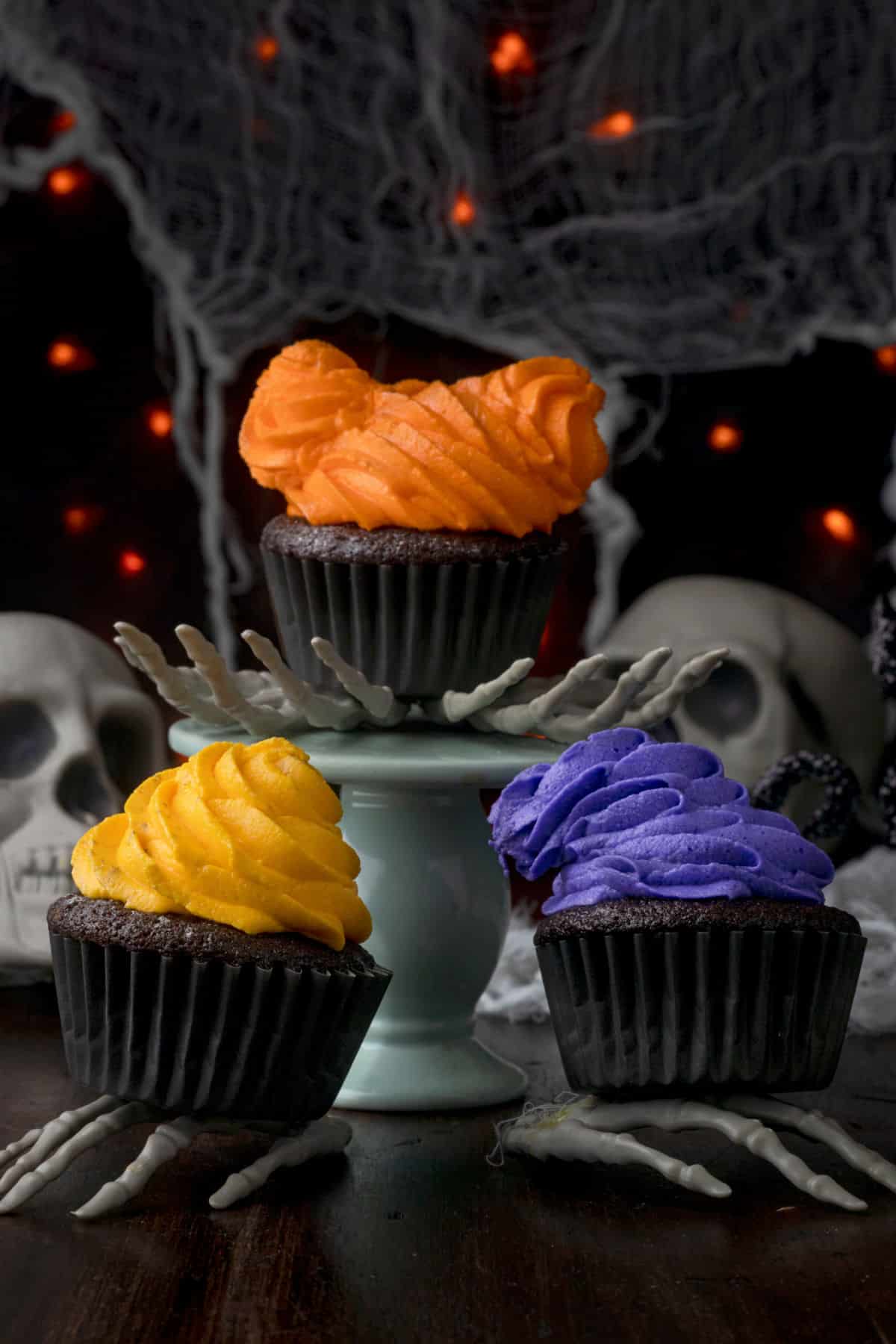 Three hocus pocus cupcakes sitting on skeleton hands. 