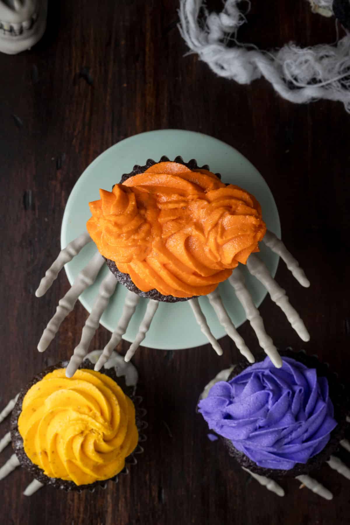 Overhead photo of three hocus pocus cupcakes next to fake cobwebs. 