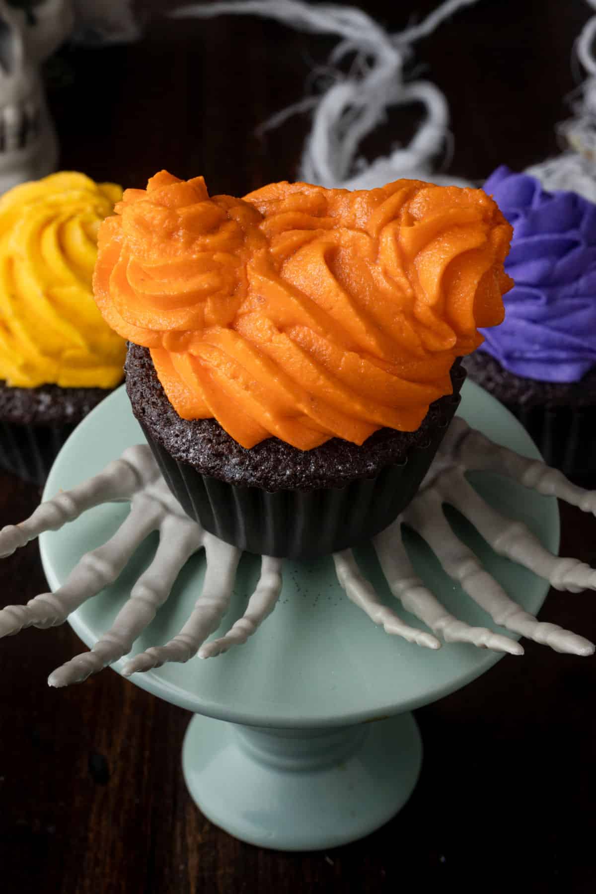 A chocolate cupcake topped with orange frosting that looks like two buns on a head. 