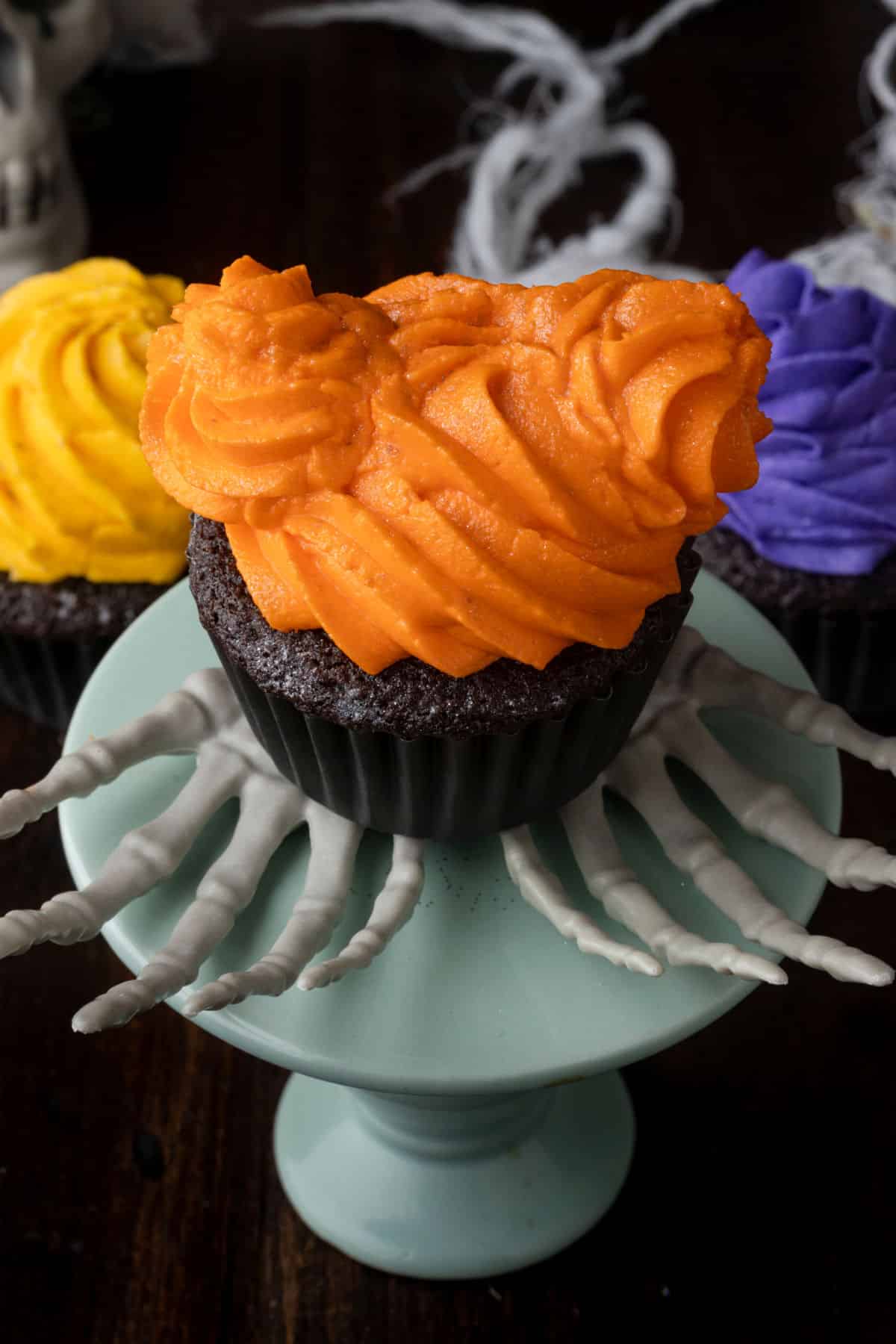 A chocolate cupcake topped with orange frosting that looks like two buns on a head.