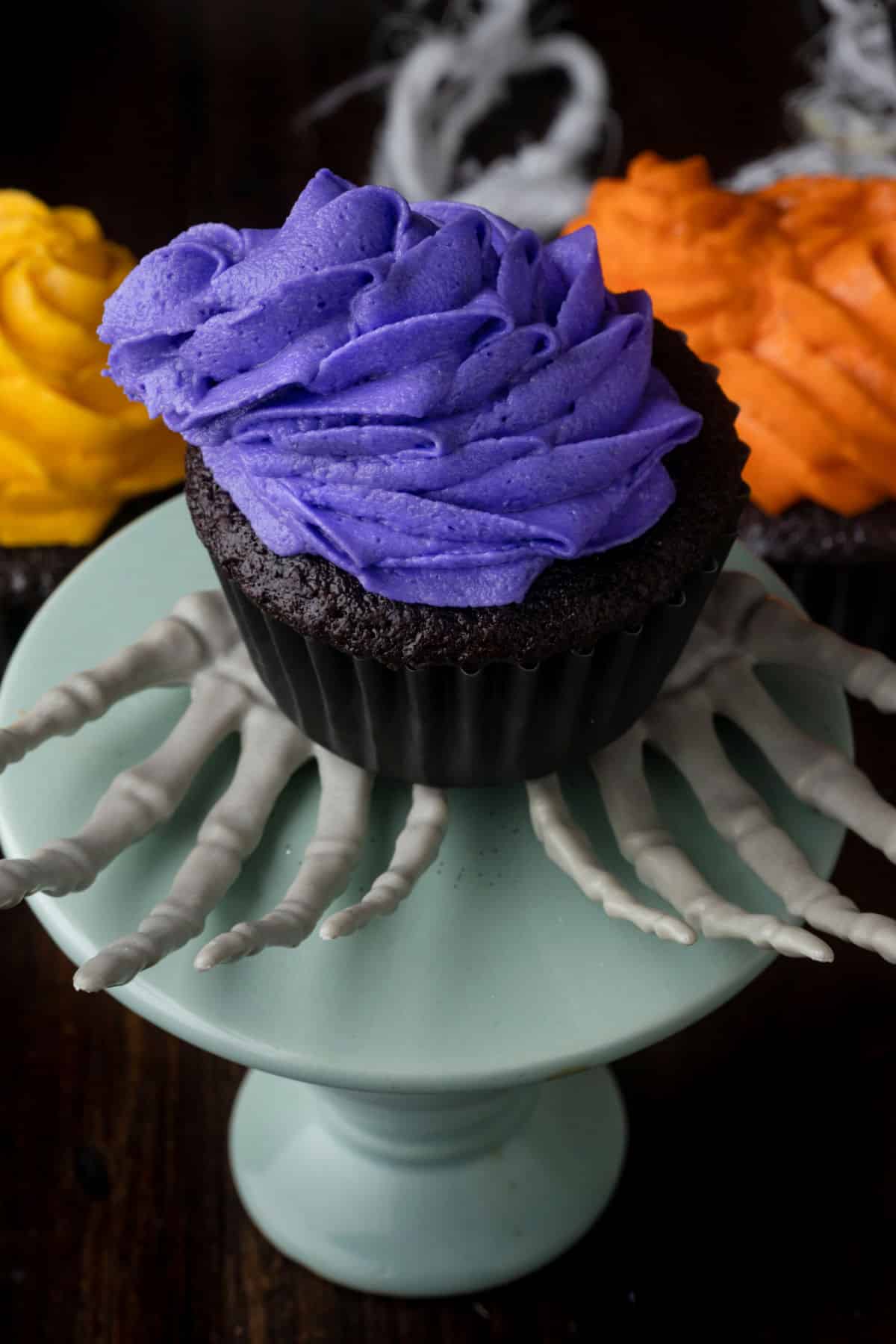 A chocolate cupcake topped with purpose frosting in a leaning cone. 