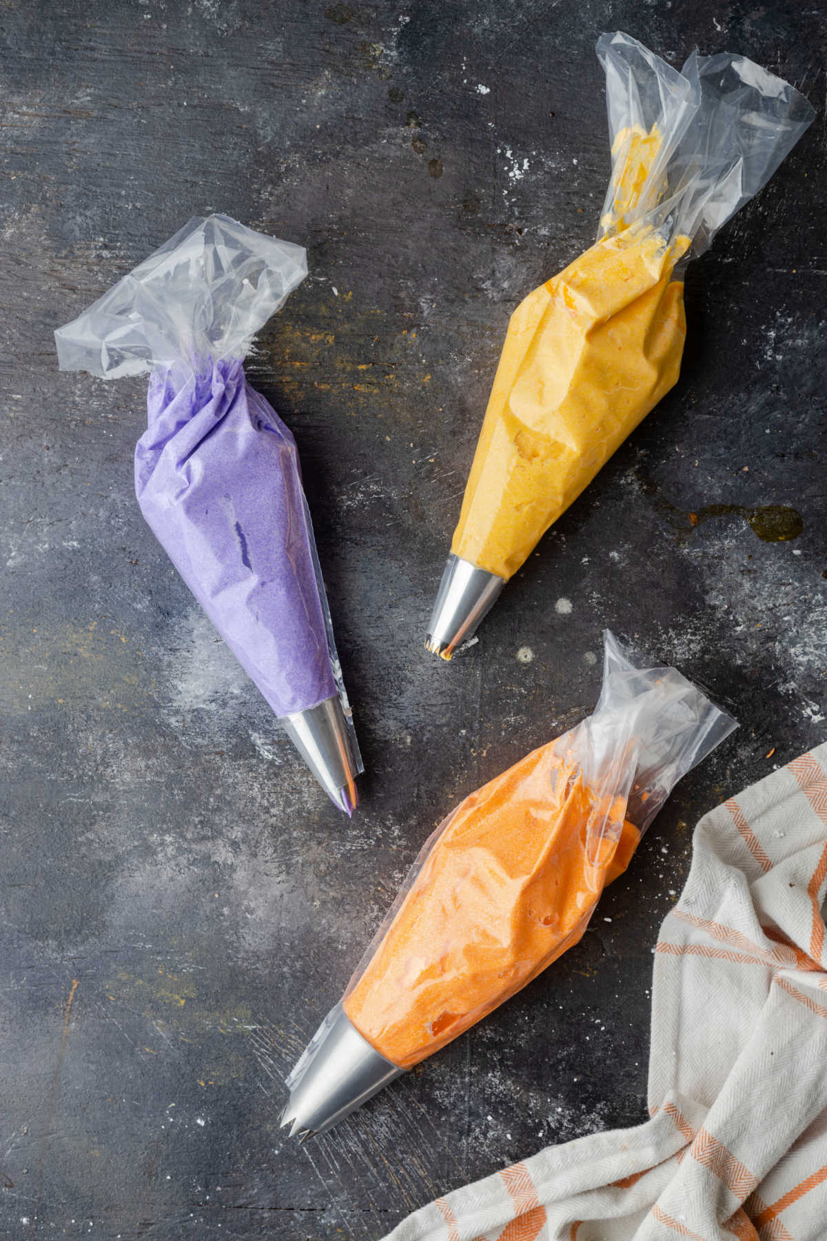 Yellow purple and orange frosting in piping bags. 