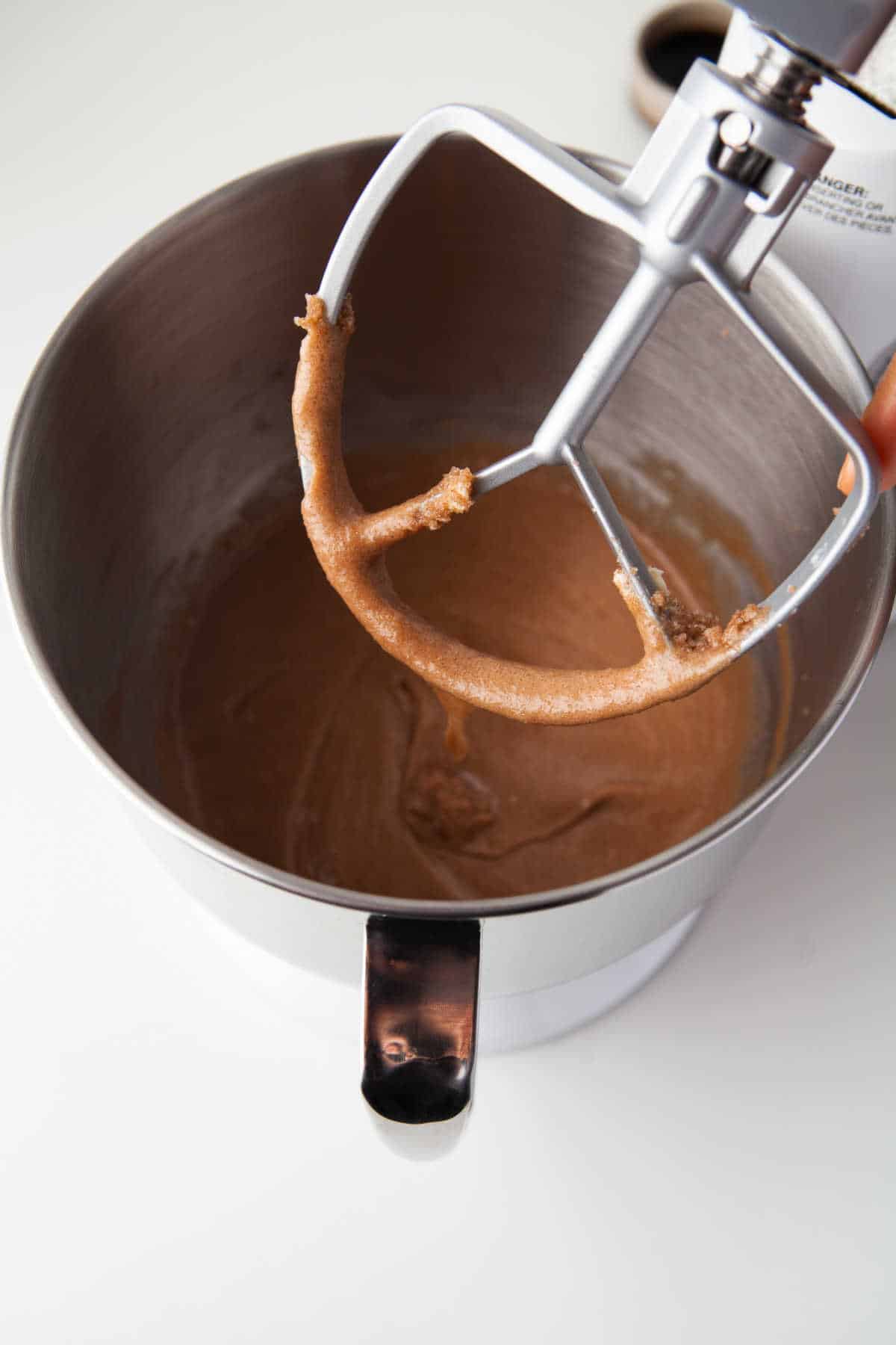 A stand mixer with a paddle attachment with eggs mixed into creamed butter and sugar.
