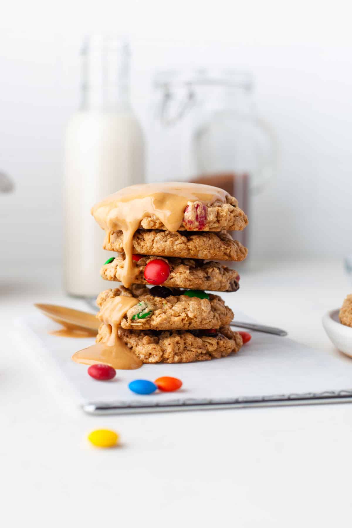 A stack of monster cookies next to a spoon with peanut butter on it.