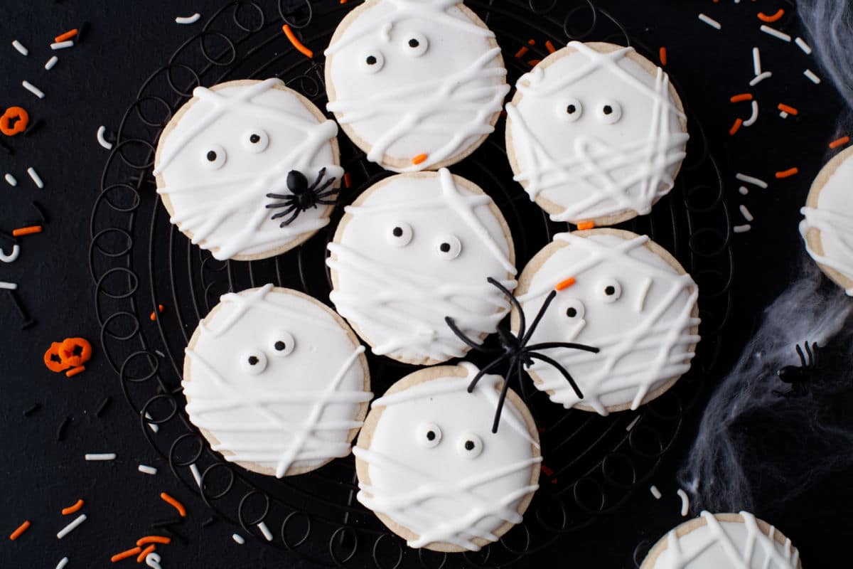 A black plate with mummy sugar cookies and plastic spiders. 