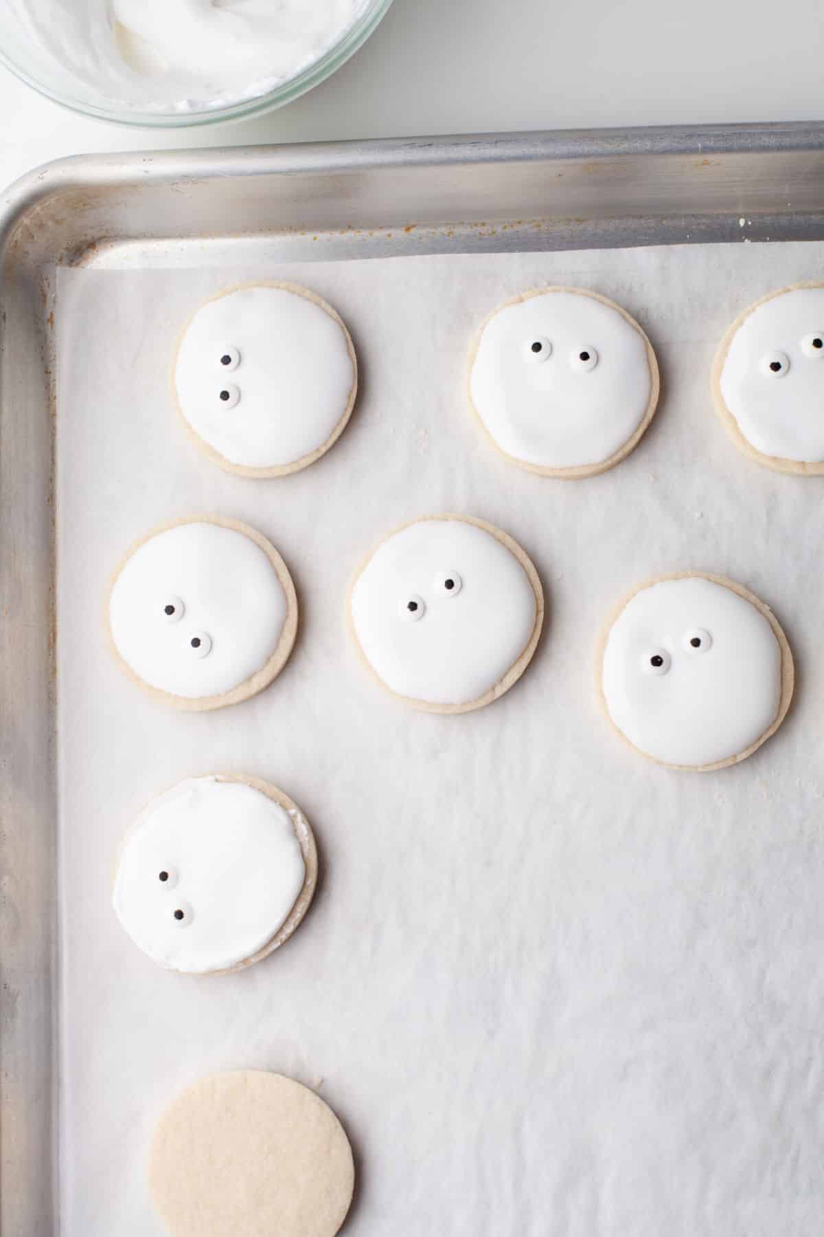 sugar cookies with candy eyes on them on a parchment lined tray.