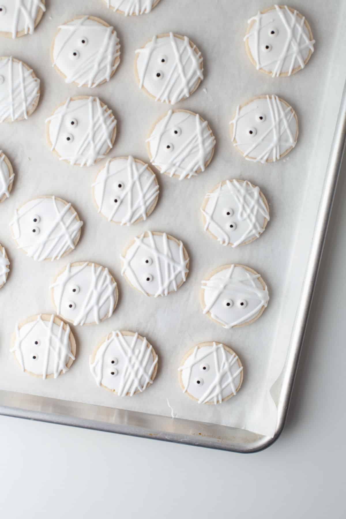 Mummy sugar cookies on a parchment paper lined tray.