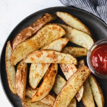 Potato wedges on a gray plate with a dish of ketchup.