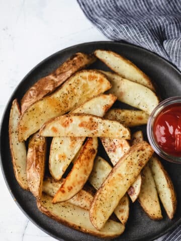 Potato wedges on a gray plate with a dish of ketchup.