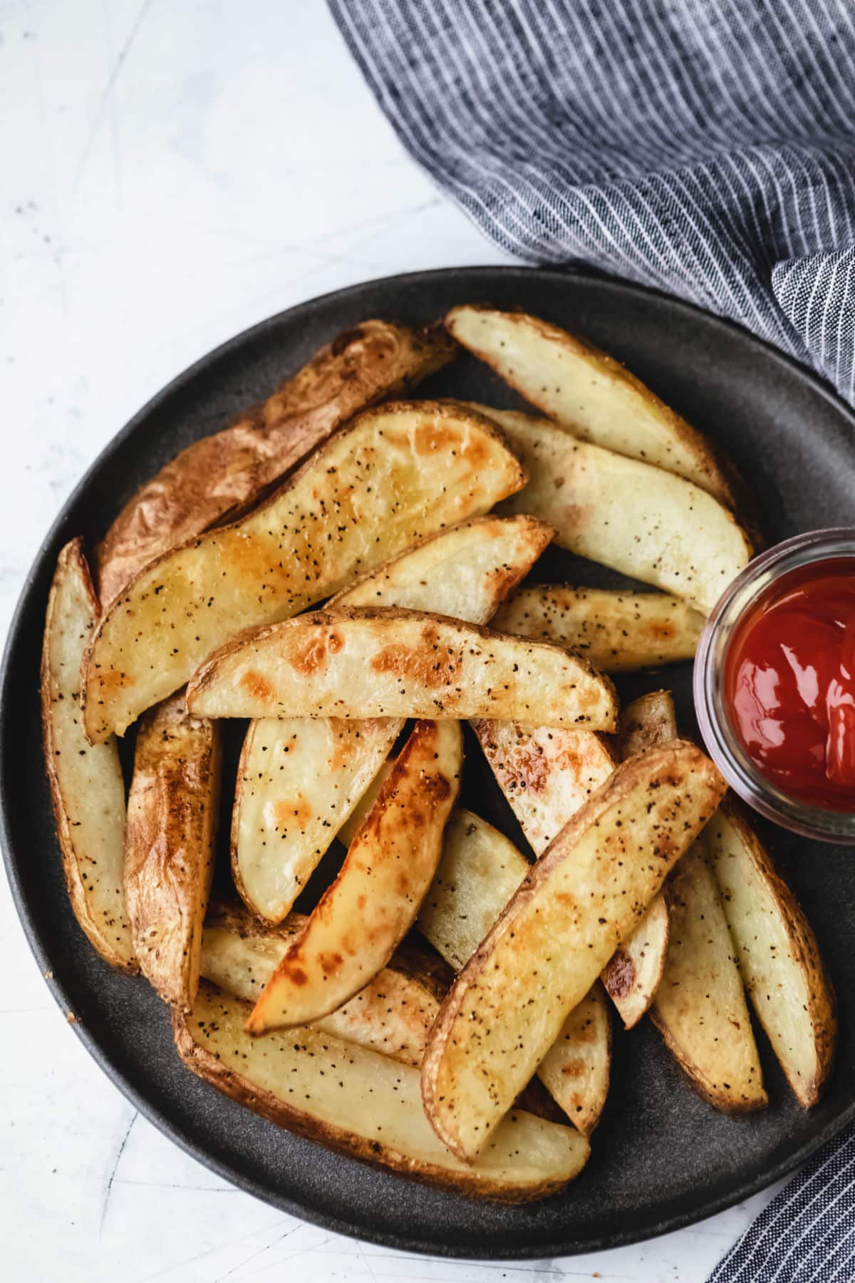 Potato wedges on a gray plate with a dish of ketchup. 