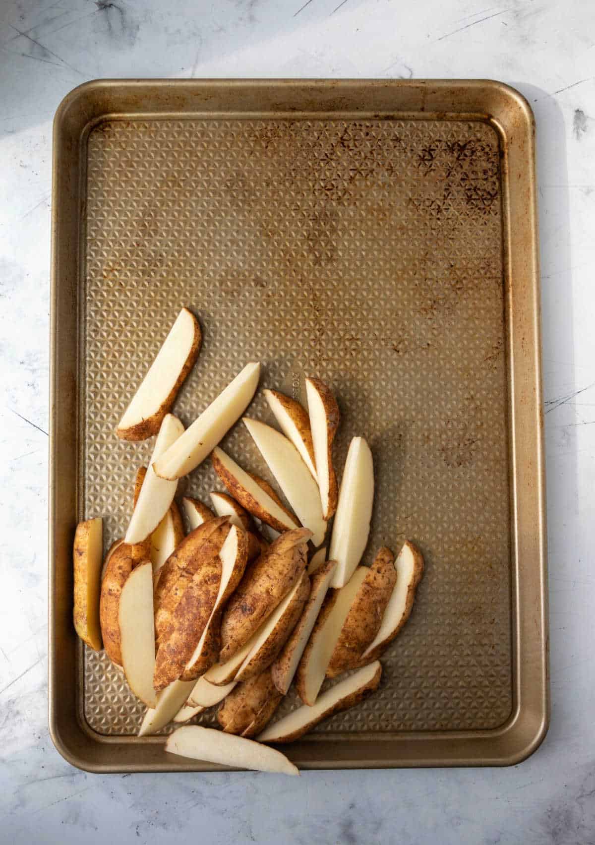 Potato wedges in a pile on a rimmed baking sheet. 