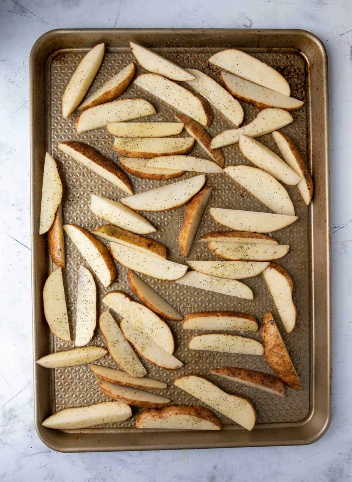 Unbaked potato wedges on a rimmed baking sheet. 